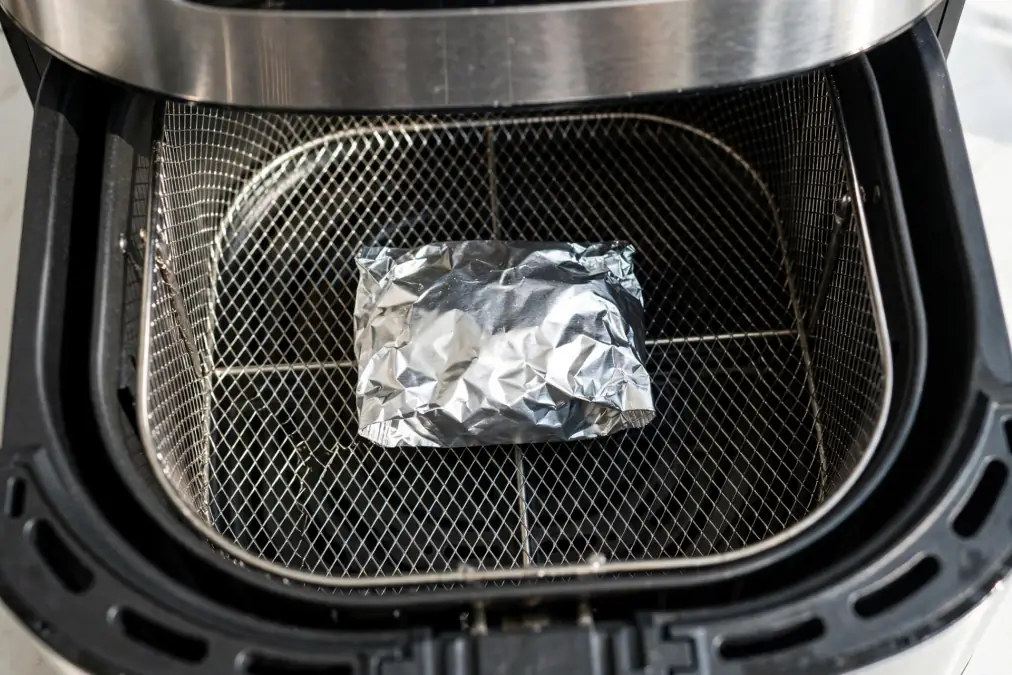 Foil packet placed in the basket of an air fryer ready for cooking