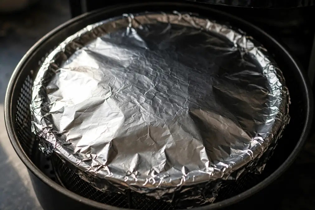 Air fryer basket fully covered with crinkled aluminum foil